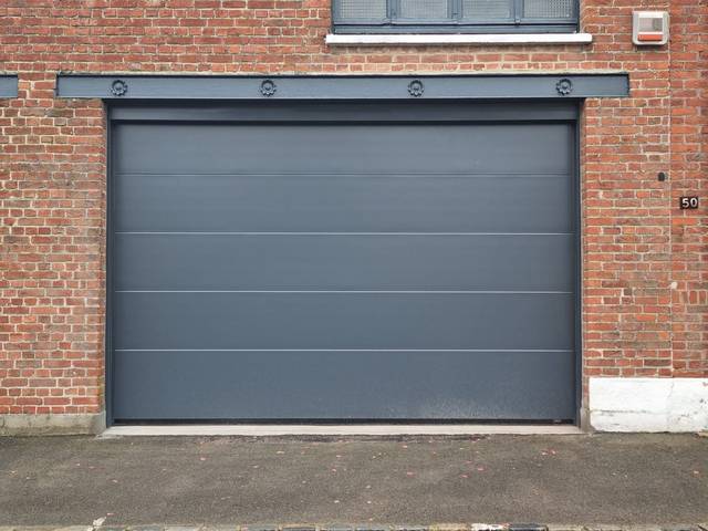 Porte de garage sectionnelle gris anthracite sur façade brique, Fermotek