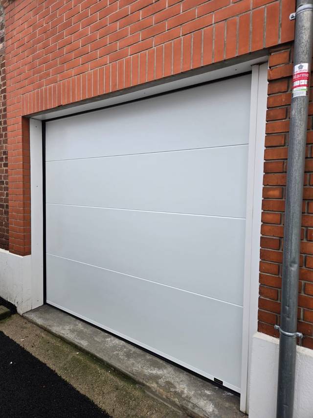Porte de garage sectionnelle claire sur façade brique, installation Fermotek